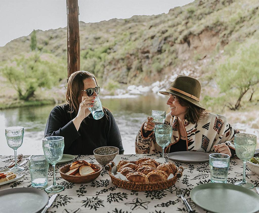 Almuerzo en la mesa larga junto al río — empanadas, copas, conversación