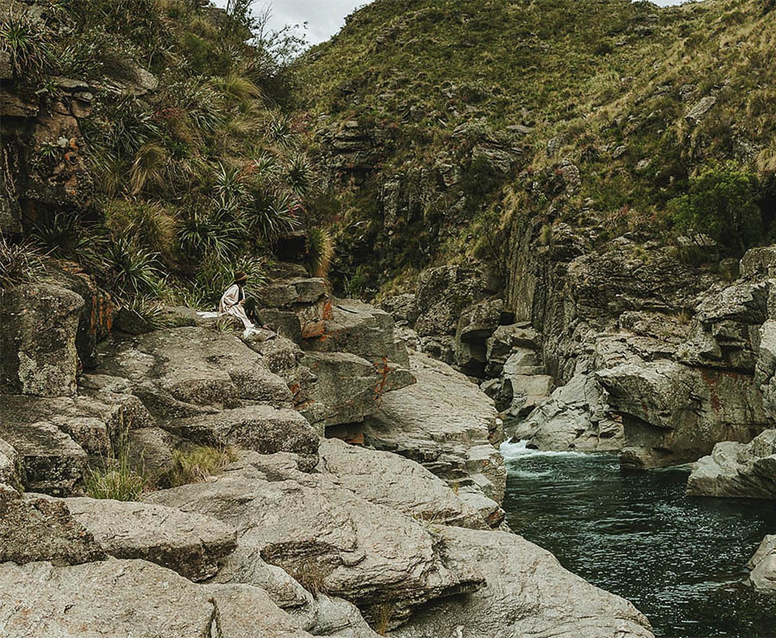 Sentada en las rocas de granito sobre un pozón profundo del río, dentro del campo